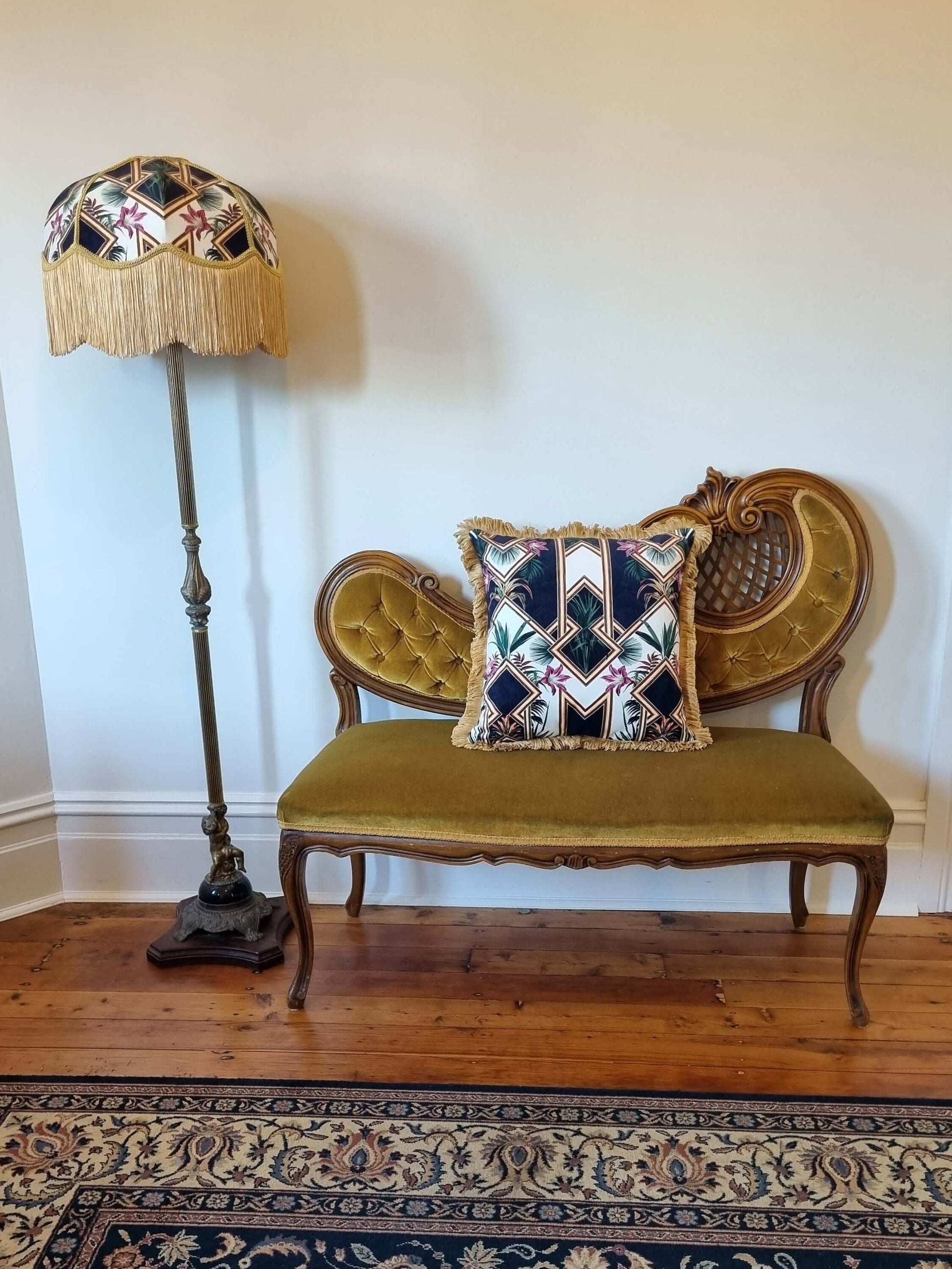 Queen K art deco cushion with geometric pattern and fringe on vintage wooden settee next to matching fringed lampshade