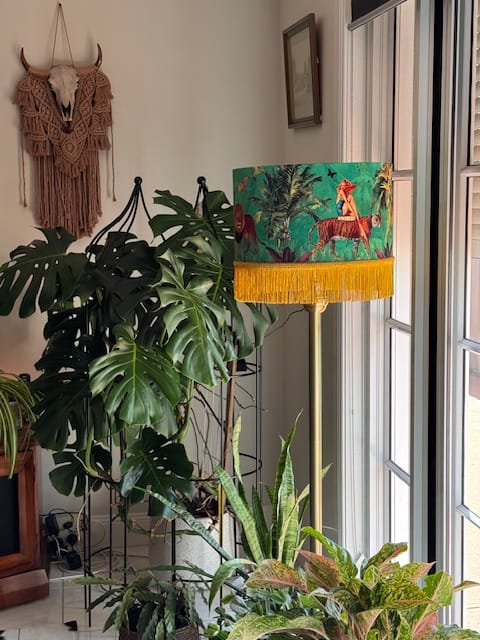 Jungle Walk Green Tassel Fringed Drum Lampshade with yellow fringe on a floor lamp near indoor plants