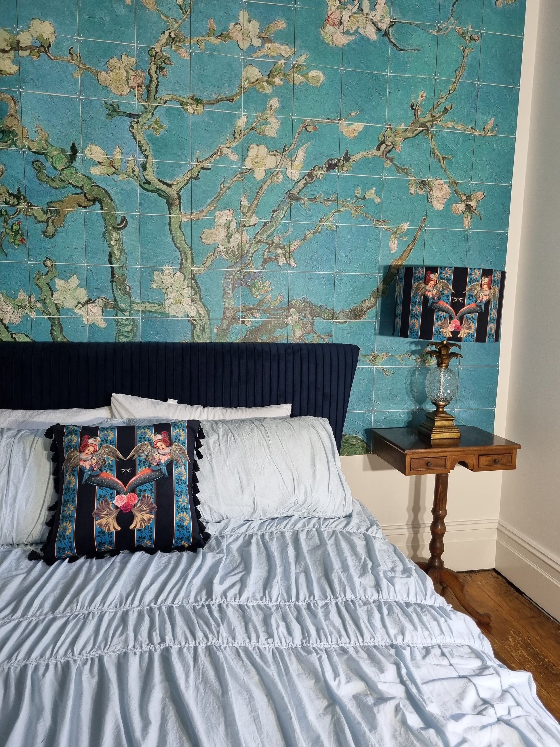 Queen K Mermaid Drum Lampshade Blue on wooden bedside table with floral blue wall and white bed linens