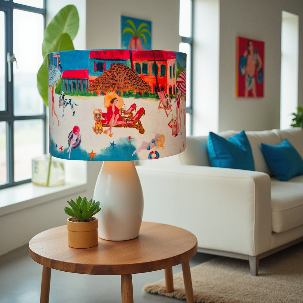 Queen K Riviera Drum Lampshade with colorful beach scene on white lamp base in living room