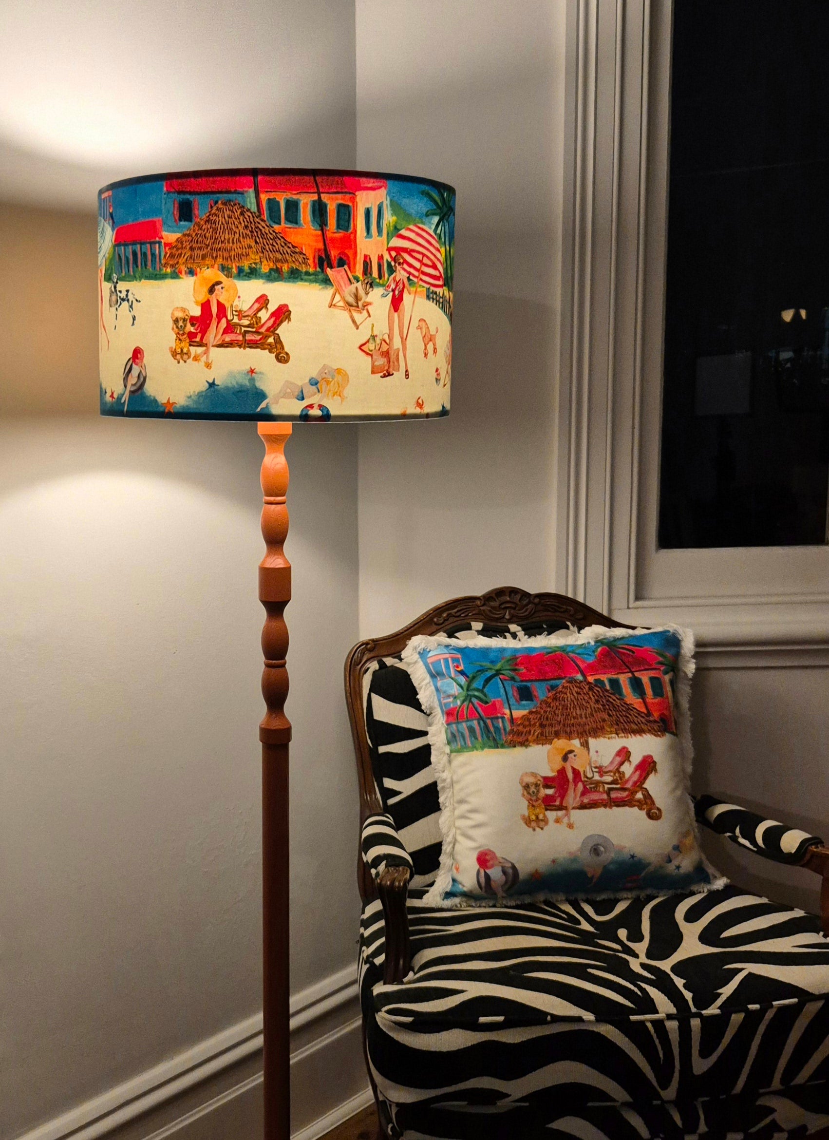 Queen K Riviera Drum Lampshade with colorful beach scene on floor lamp next to zebra print chair and matching pillow