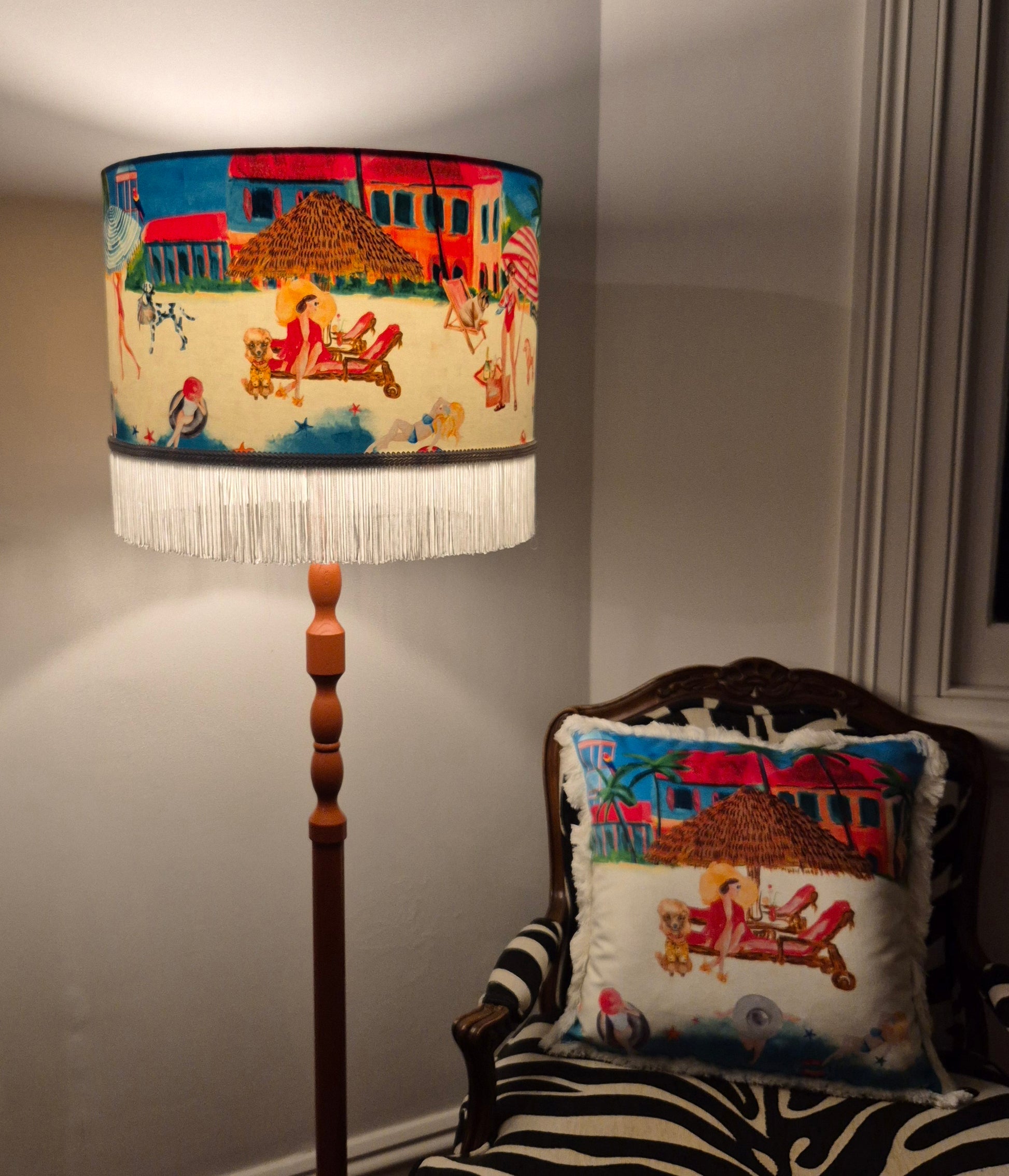 Queen K Riviera Fringed Drum Lampshade with colorful beach scene and white fringe on wooden floor lamp