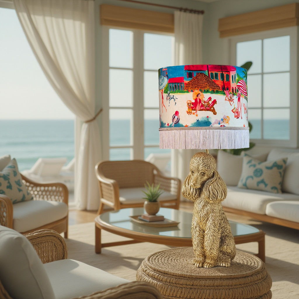 Riviera Fringed Drum Lampshade with colorful beach scene on gold dog-shaped base in bright coastal living room