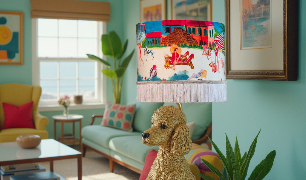 Queen K Riviera Fringed Drum Lampshade with colorful coastal artwork and white fringe in a bright living room