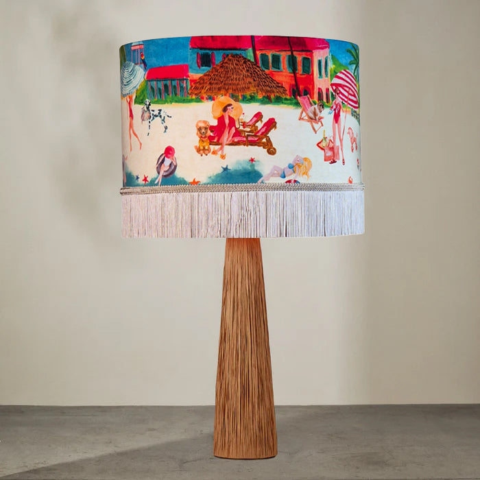 Queen K Riviera Fringed Drum Lampshade with colorful beach scene and white fringe on wooden lamp base