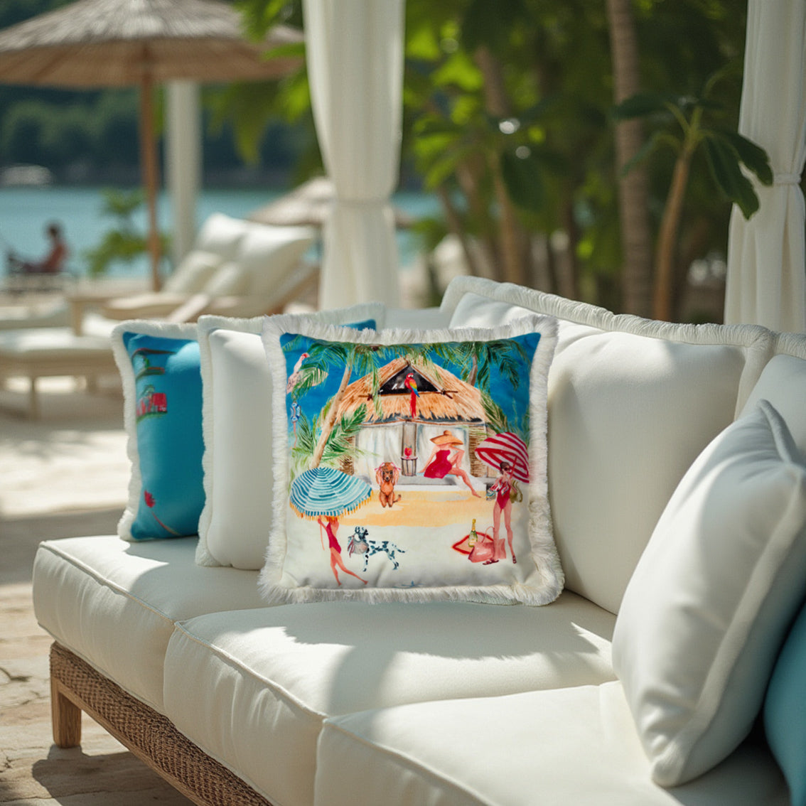 Queen K Riviera Fringed Velvet Cushion with colorful beach scene on white outdoor sofa