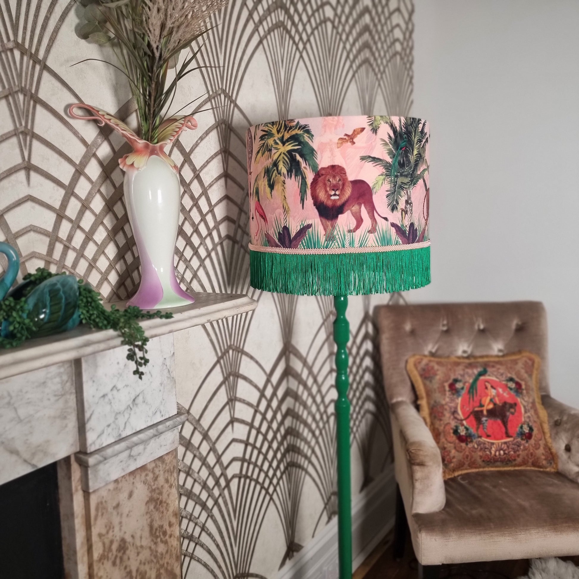 Queen K Jungle Walk Pink Fringed Drum Lampshade with green fringe on a green floor lamp in a vintage-style living room